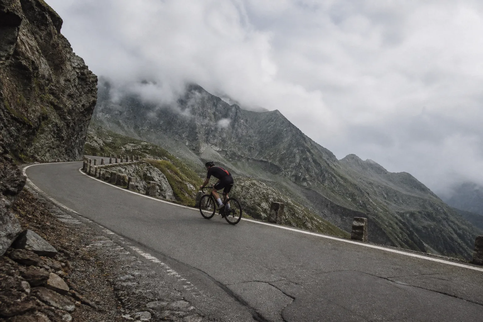 Lone road cyclist climbing a high mountain switchback beneath low cloud