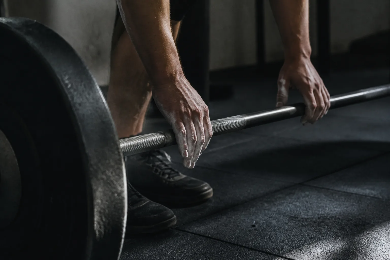Athlete setting chalked hands on a barbell in a dark training space